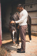 LORËVEN Drift Stretch Trouser in Anchor Charcoal — man in a white long-sleeve sweater standing with a horse in a rustic stable
