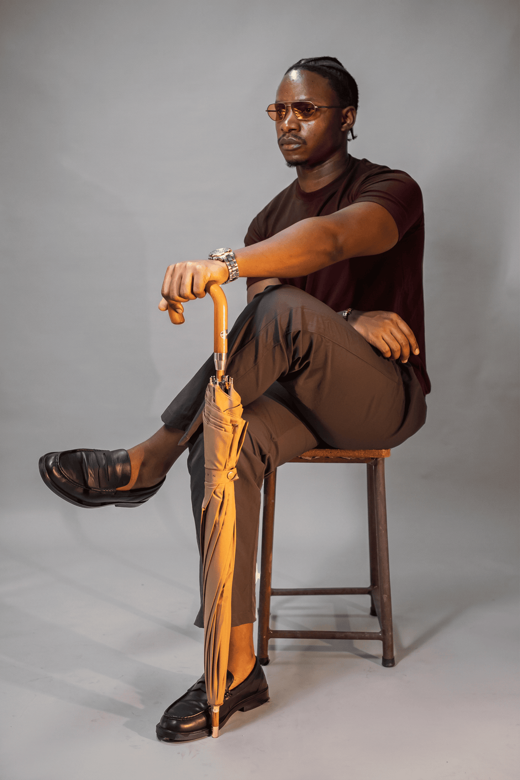 LORËVEN Drift Stretch Trouser in Anchor Charcoal — man seated on a wooden stool holding a closed umbrella against a grey studio background