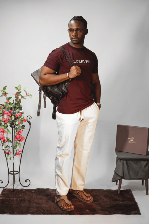 LORËVEN Drift Stretch Trouser in Chalk White — man in a maroon LORËVEN t-shirt with drawstring trousers and a black shoulder bag against a light studio background