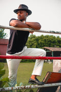 LORËVEN Drift Stretch Trouser in Chalk White — man in a black fedora hat and t-shirt leaning against a weathered metal fence outdoors