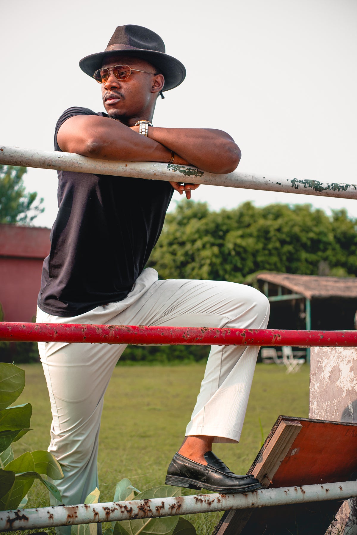 LORËVEN Drift Stretch Trouser in Chalk White — man in a black fedora hat and t-shirt leaning against a weathered metal fence outdoors