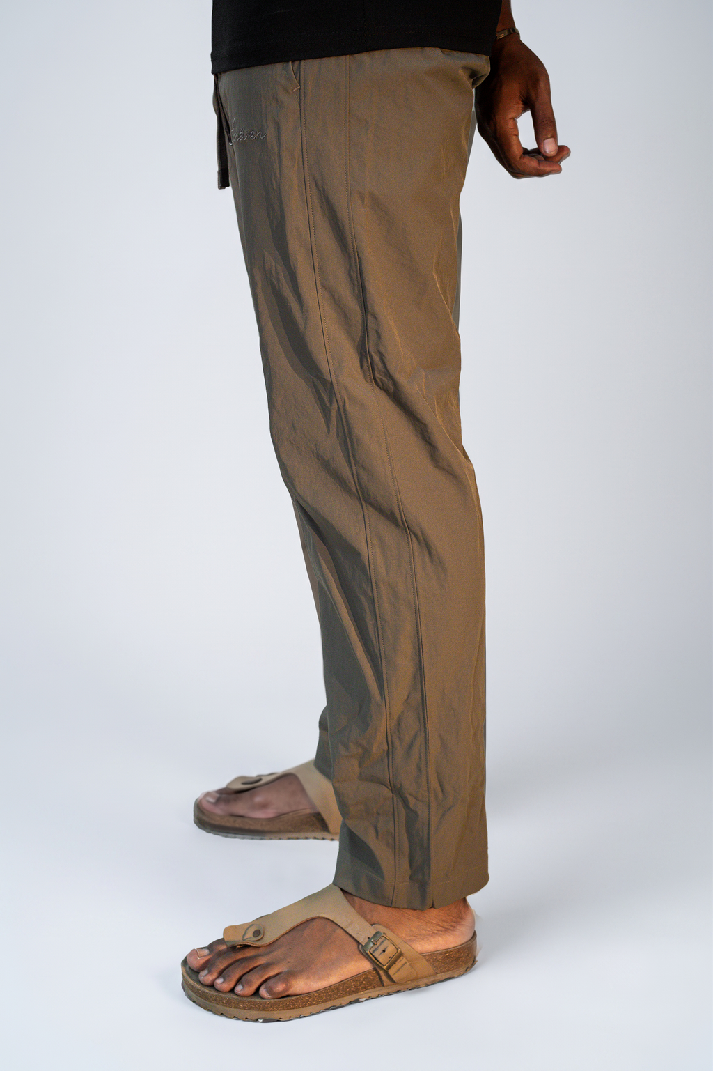 LORËVEN Drift Stretch Trouser in Mouse Brown — side profile close-up of the trouser leg and tan leather slide sandals against a light grey studio background