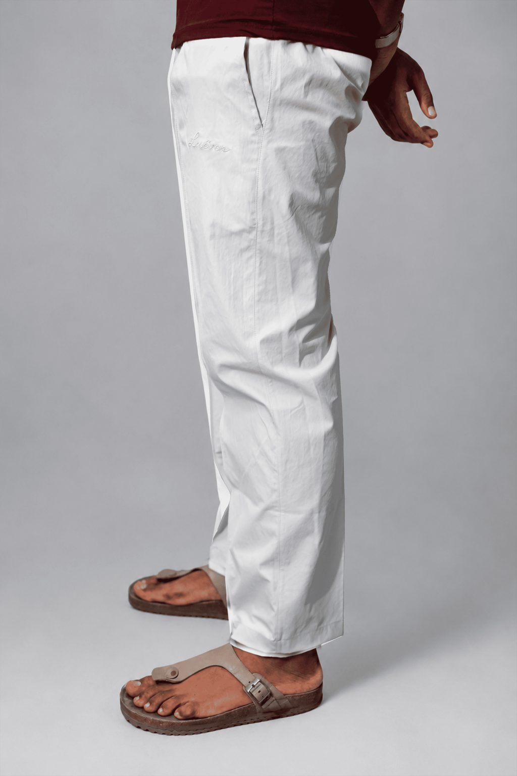 LORËVEN Fold Stretch Trouser in Chalk White — close-up of the trousers from the waist down with brown leather slide sandals against a neutral grey studio background