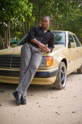 LORËVEN Striped Linen Trouser in Mediterranean Olive — man in a black button-down shirt leaning against a vintage yellow Mercedes-Benz sedan on a dirt path amid trees