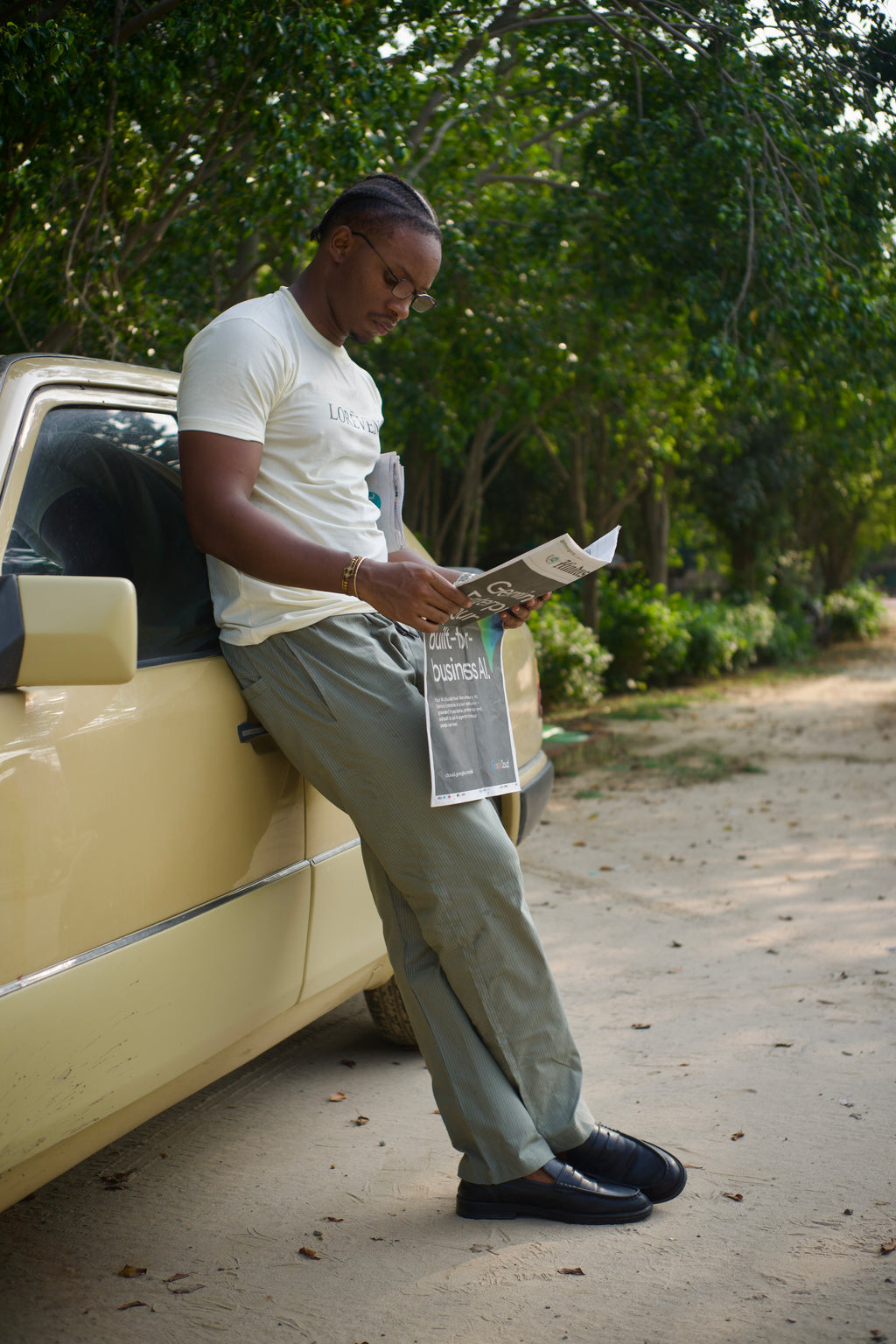 LORËVEN Striped Linen Trouser in Rosemary — man in a white t-shirt reading a newspaper while leaning against a cream vintage car on a dirt road amid trees