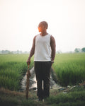 LORËVEN Linen Cotton Trouser in Deep Olive — man in a white tank top standing on a rural field path at golden hour, holding a closed umbrella
