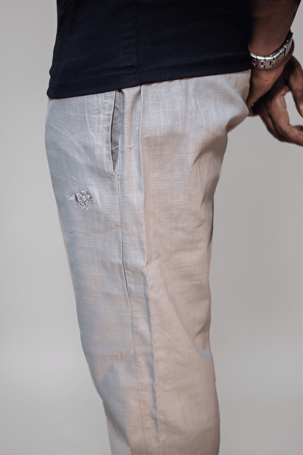 LORËVEN Linen Cotton Trouser in Silver Moon grey — close-up of the linen fabric and tonal embroidered mark on the thigh, paired with a dark shirt and silver watch