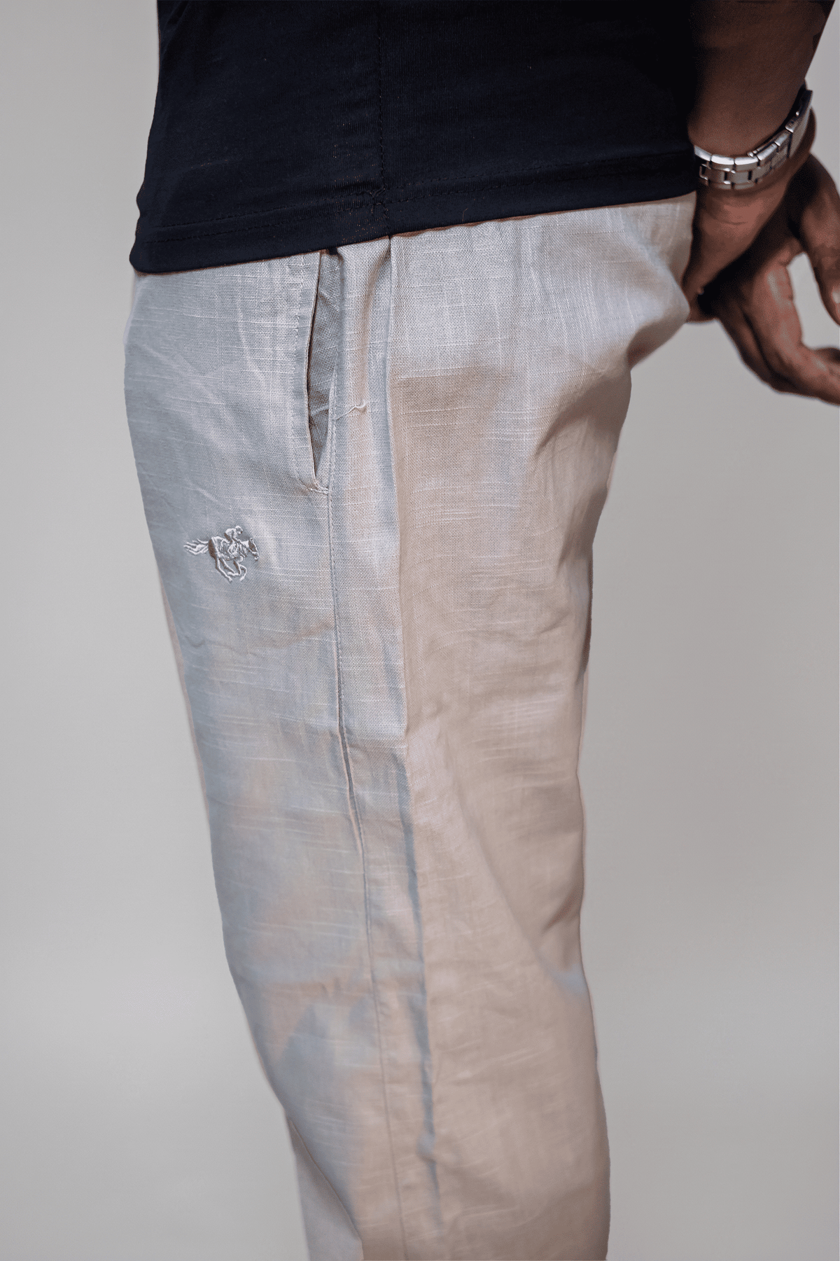 LORËVEN Linen Cotton Trouser in Silver Moon grey — close-up of the linen fabric and tonal embroidered mark on the thigh, paired with a dark shirt and silver watch