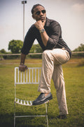 LORËVEN Striped Linen Trouser in Dune Beige — man in sunglasses and a black shirt seated on a white metal chair in an outdoor grassy field