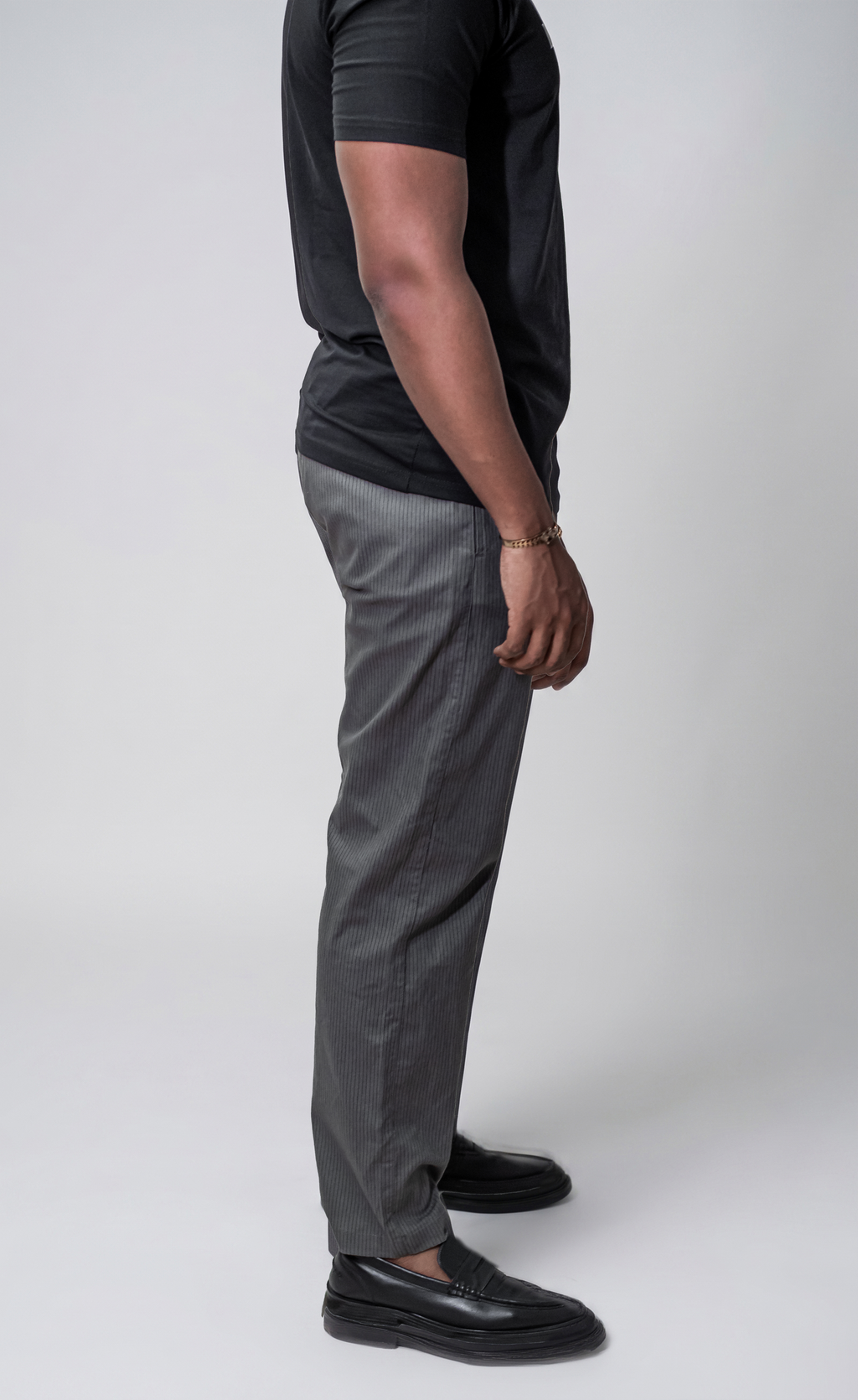 LORËVEN Striped Linen Trouser in Mediterranean Olive — side-profile view of a man in a black t-shirt and black leather loafers against a light grey studio background