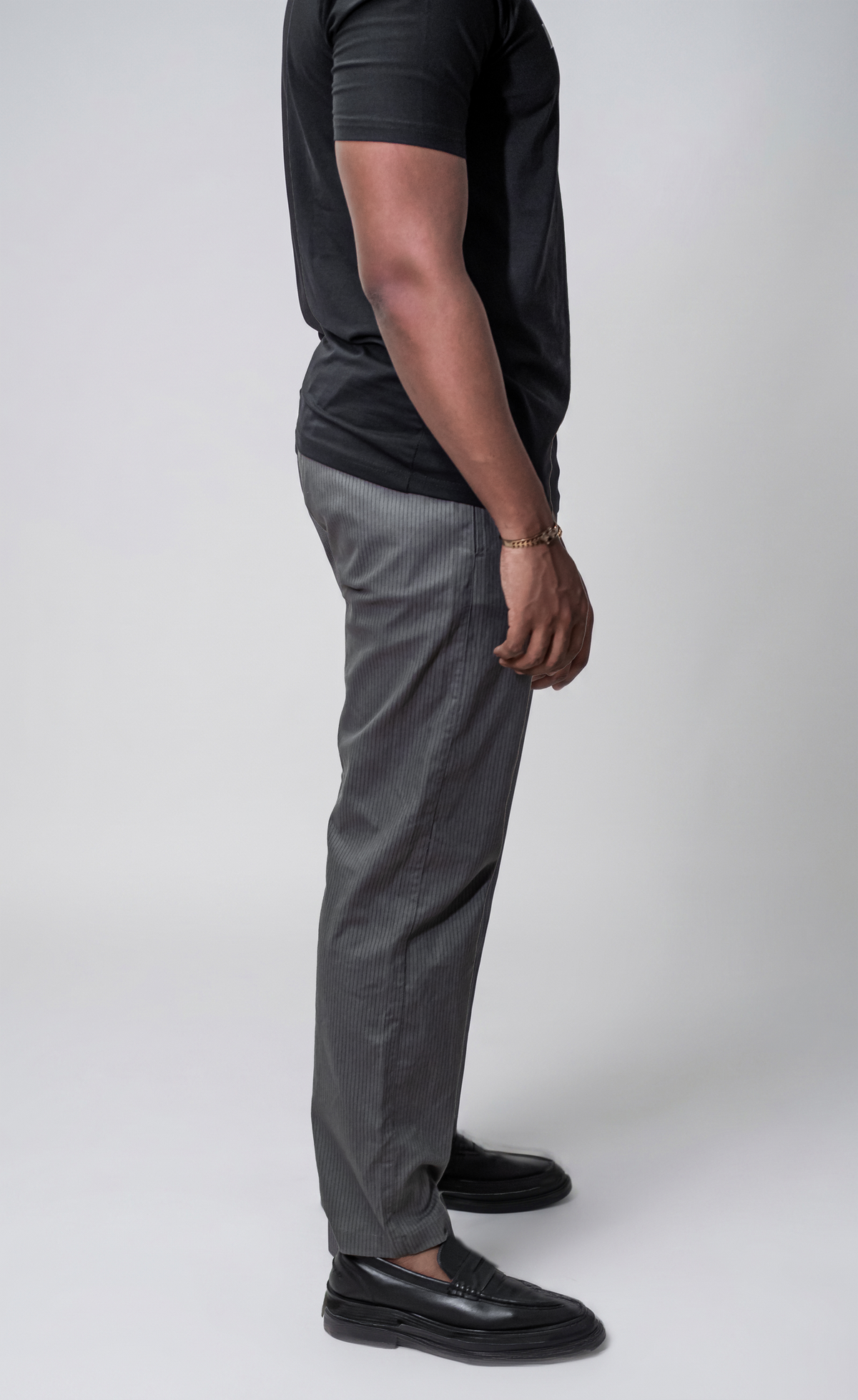 LORËVEN Striped Linen Trouser in Mediterranean Olive — side-profile view of a man in a black t-shirt and black leather loafers against a light grey studio background