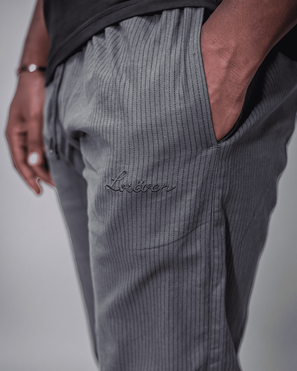 LORËVEN Striped Linen Trouser in Mediterranean Olive — close-up of the fabric texture and side pocket with an embroidered LORËVEN script logo on the thigh