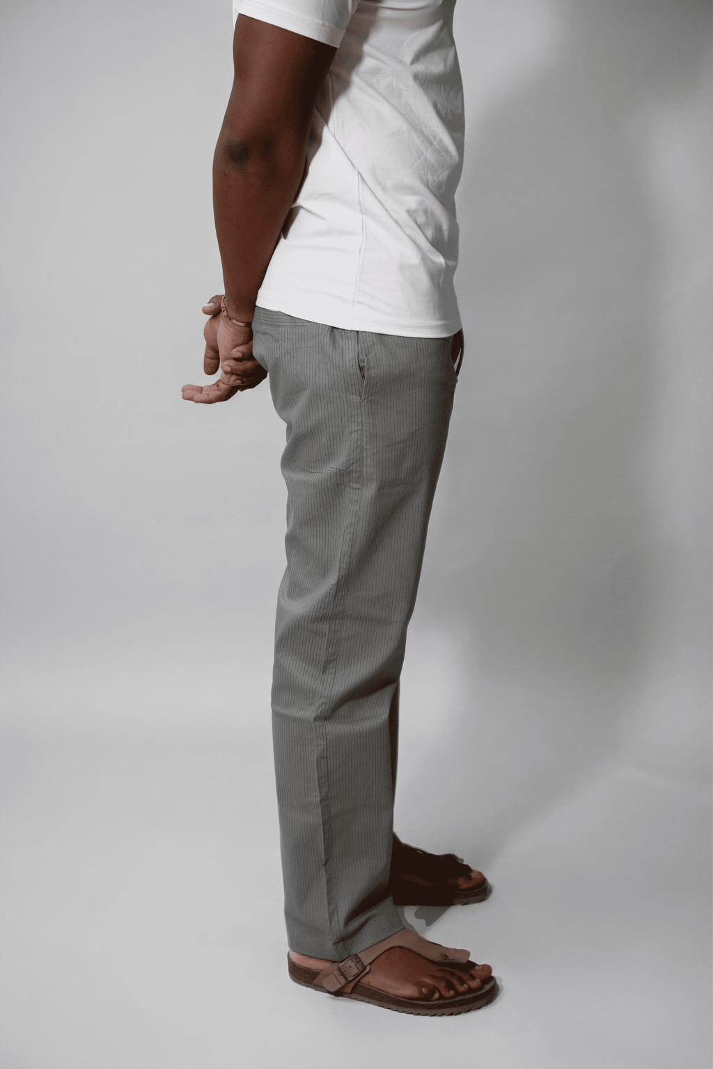 LORËVEN Striped Linen Trouser in Rosemary — side view of a man in a white t-shirt and brown leather slide sandals against a light grey studio background