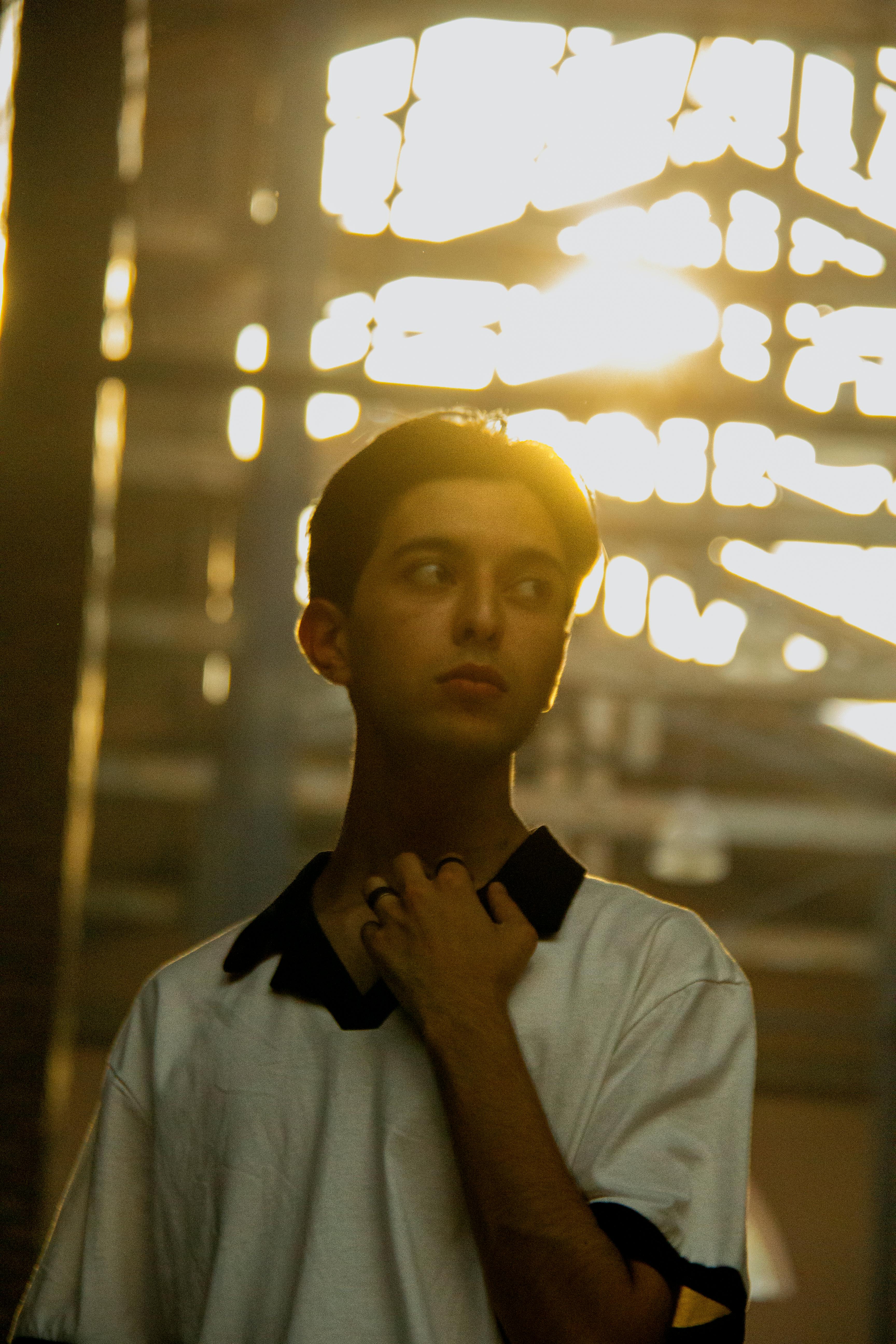 Men’s white polo shirt with black collar detail styled in warm indoor sunlight