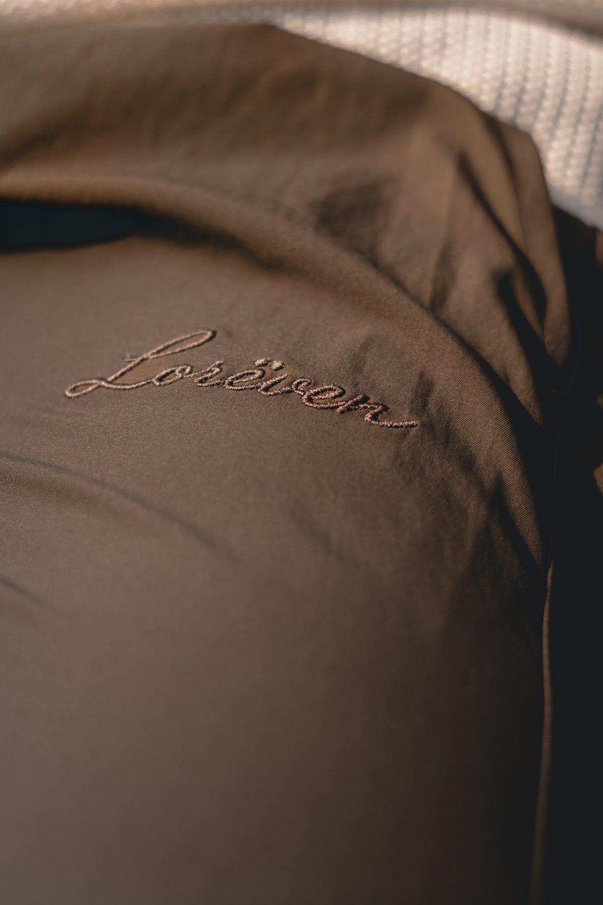 Close-up of LORËVEN leisure trouser in soft brown nylon with the Lorëven script embroidered in tonal thread