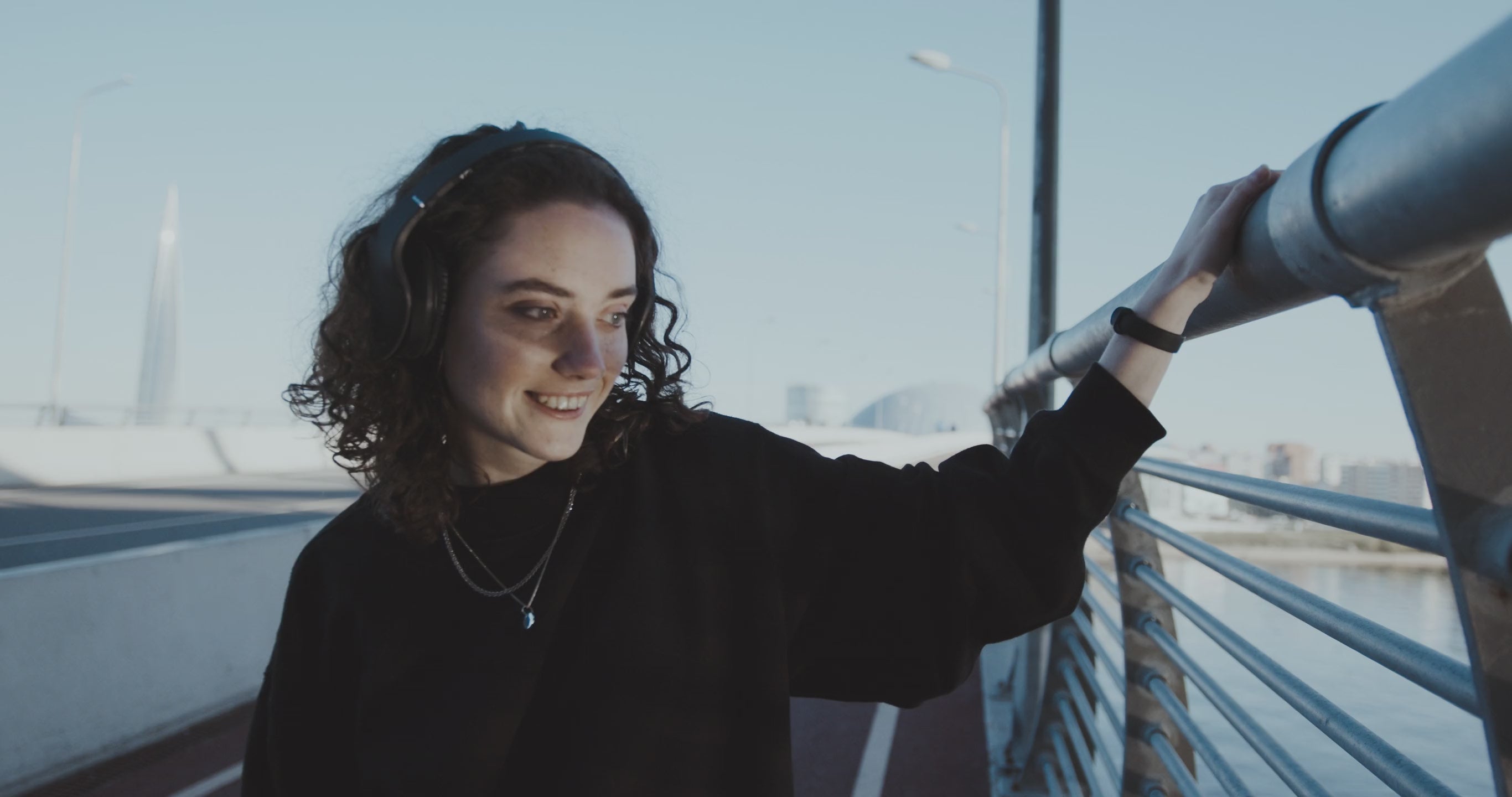 Video showcasing new arrivals with a woman in a black sweater and silver necklace on a modern city bridge