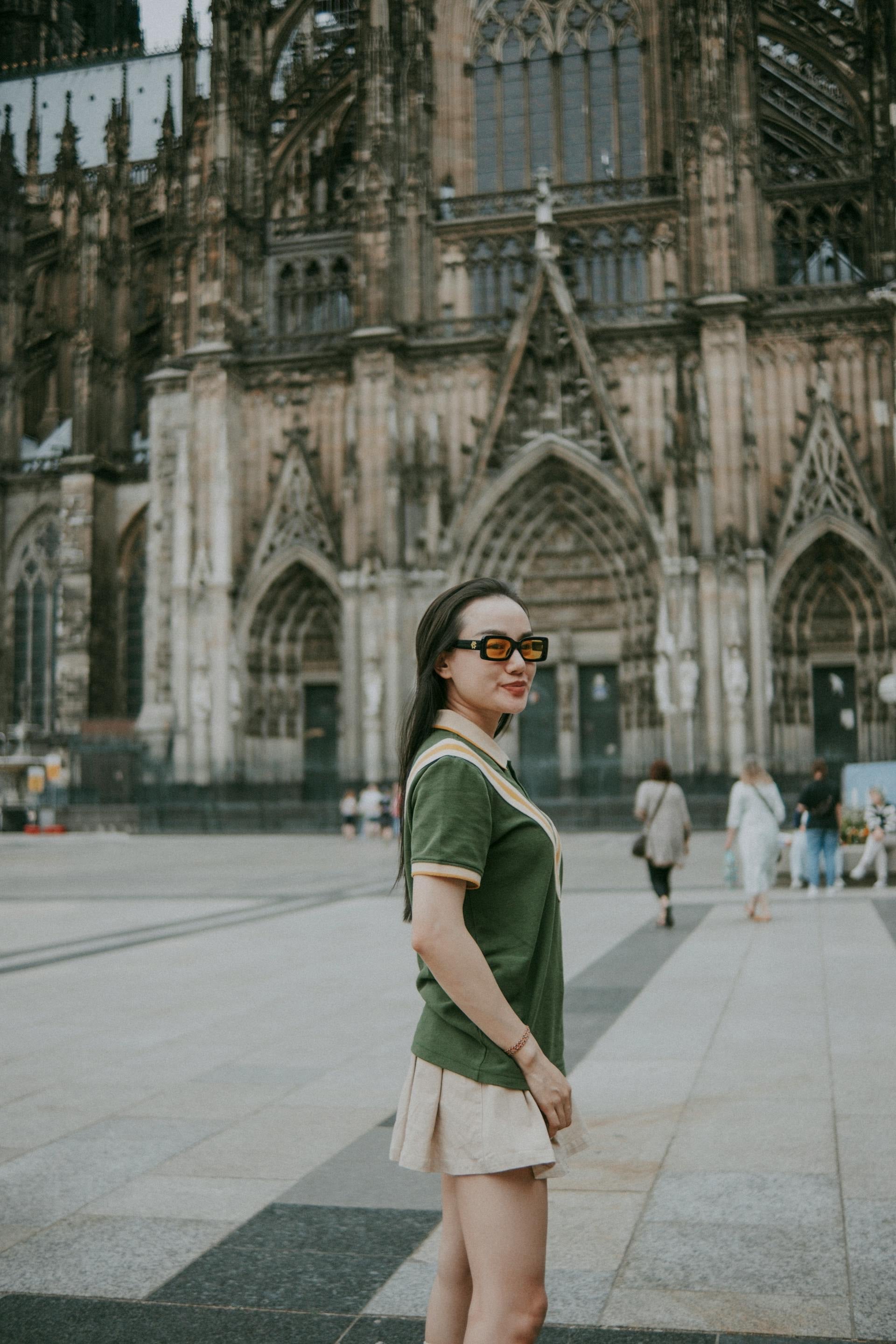 Woman wearing a green polo shirt with beige skirt and sunglasses standing outdoors in front of a historic cathedral
